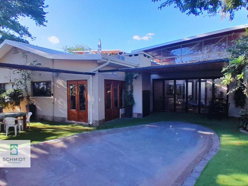 Rear view of the property featuring a covered patio area, glass sliding doors, and a paved outdoor space set within a landscaped garden.