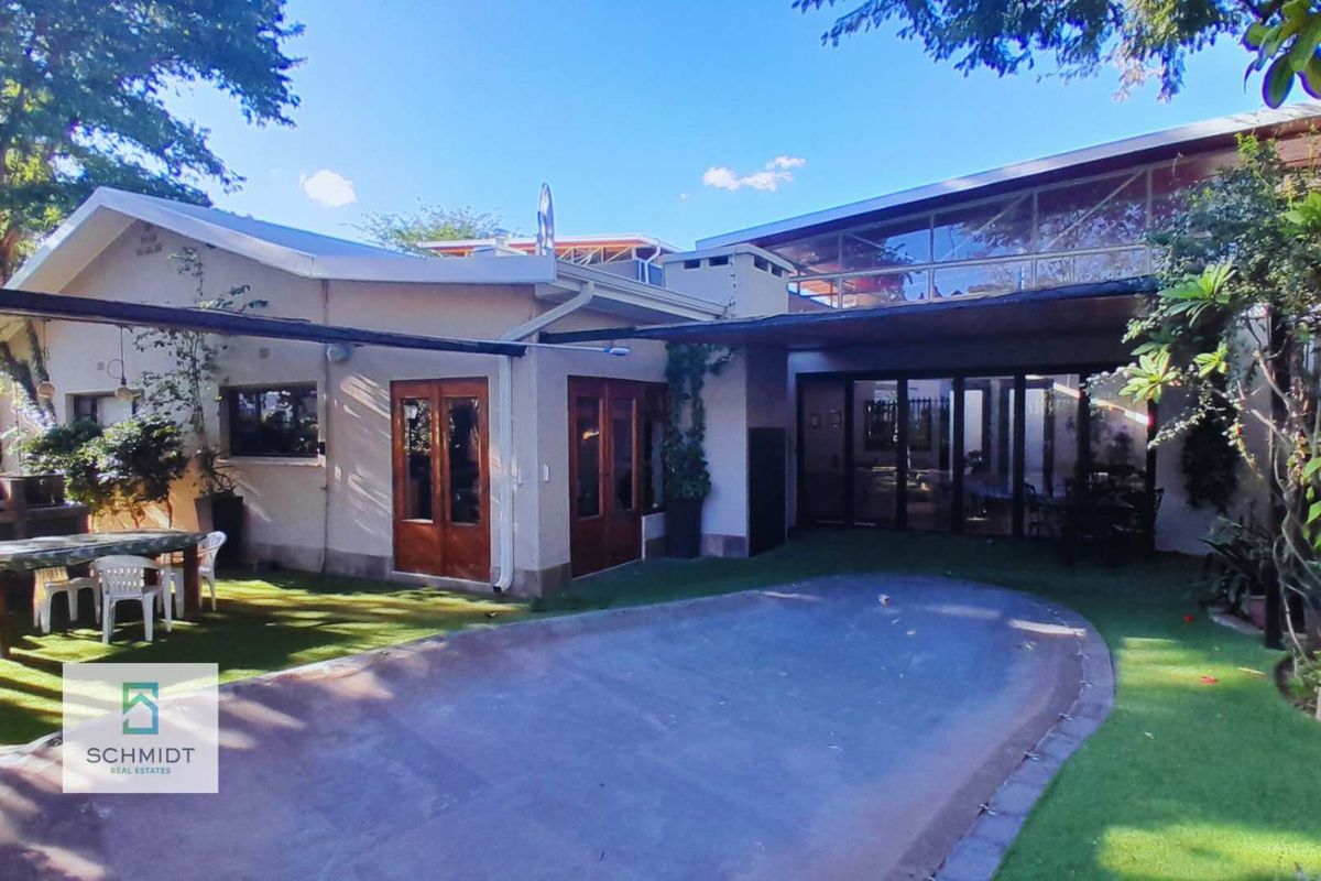 Rear view of the property featuring a covered patio area, glass sliding doors, and a paved outdoor space set within a landscaped garden.