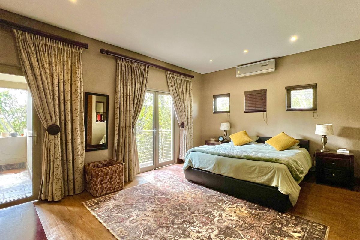 Spacious bedroom featuring wood-look flooring, recessed ceiling lighting, a wall-mounted air conditioning unit, and direct access to a private balcony through glass doors.