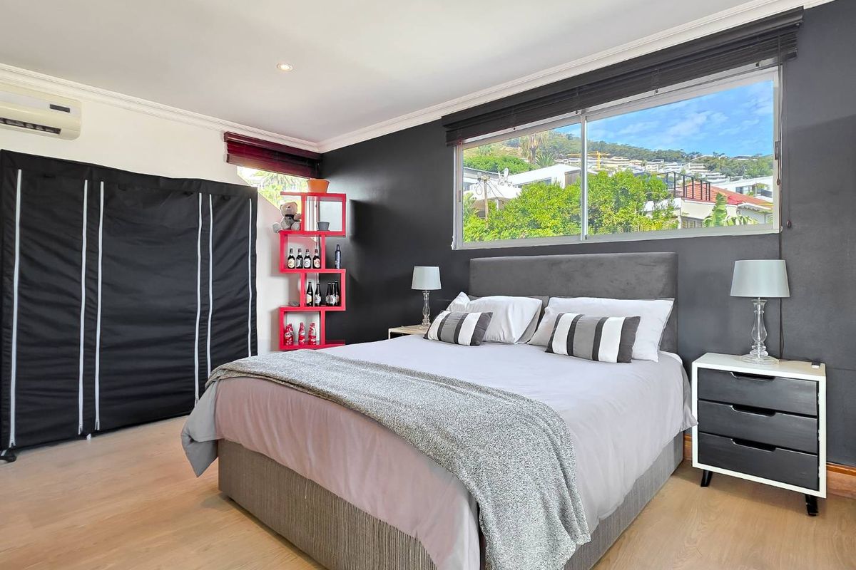 A well-lit bedroom featuring laminate flooring, recessed downlighting, air conditioning, and a large window with views of the surrounding neighborhood.