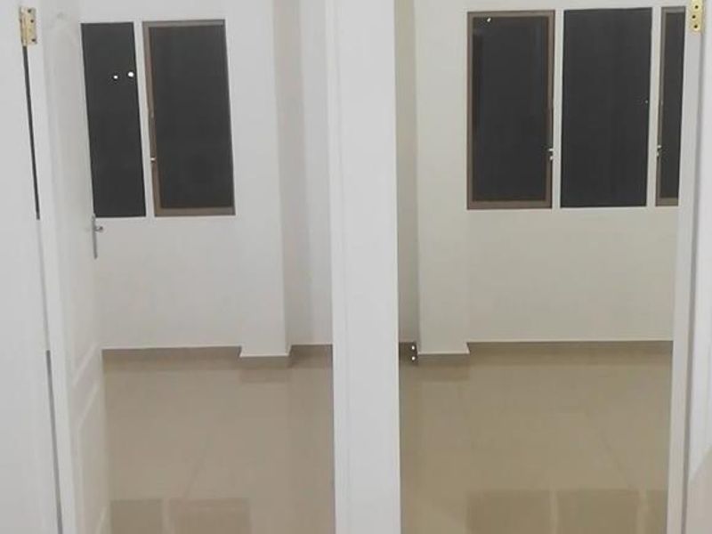 A bright, empty hallway featuring neutral tiled flooring and two doorways leading into adjacent rooms with large windows.