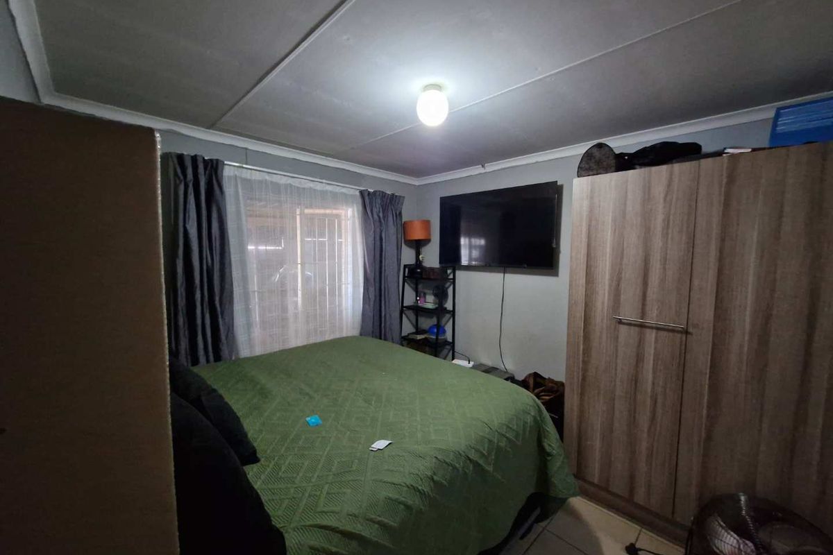 A functional bedroom featuring tiled flooring, a ceiling-mounted light fixture, and a window with curtain tracks.