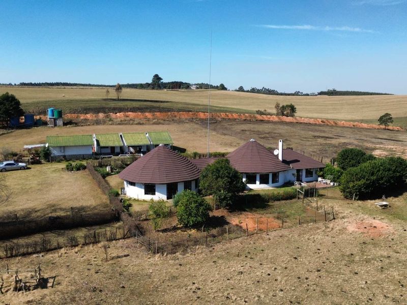 Aerial view of a farm property featuring multiple structures with thatched roofs, surrounding fencing, and open landscape.