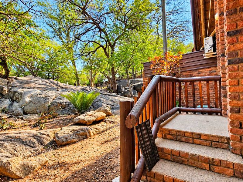 A rustic outdoor patio area featuring exposed brick walls, timber railings, and concrete steps, set against a natural rocky landscape.