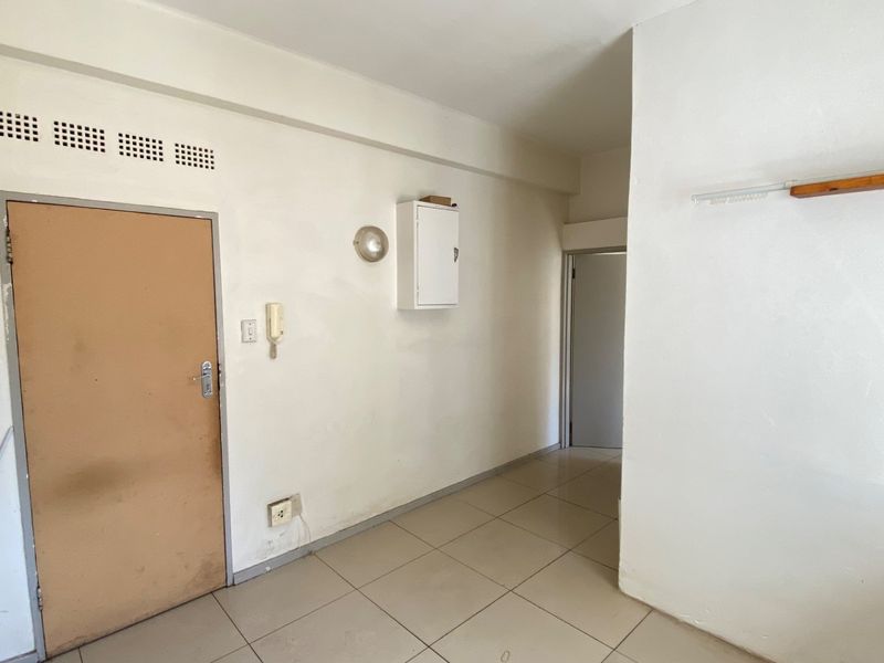 A vacant hallway featuring tiled flooring, an intercom system, and a wall-mounted distribution board, presenting a blank canvas for interior updates.