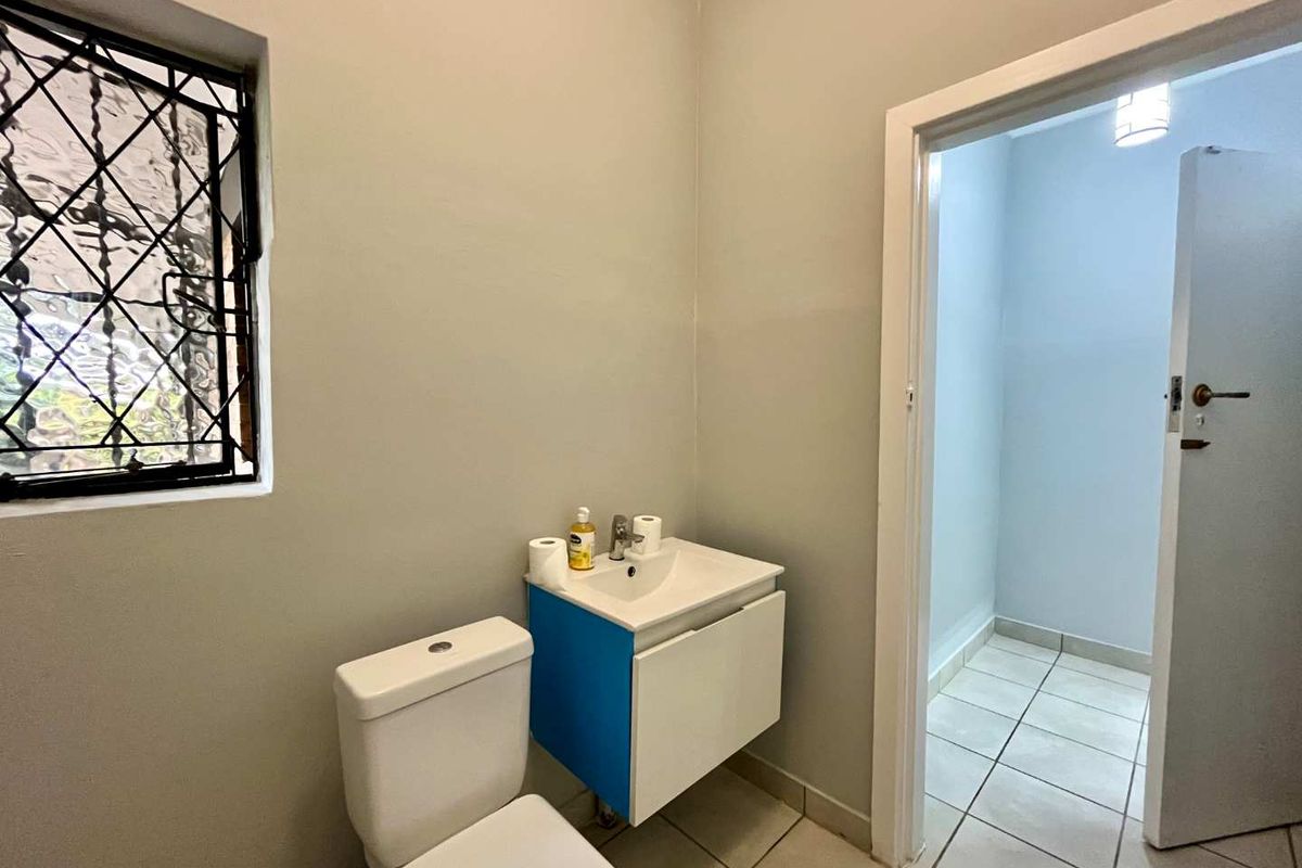 A functional bathroom featuring a wall-mounted vanity with basin, toilet, tiled flooring, and a window with security bars.
