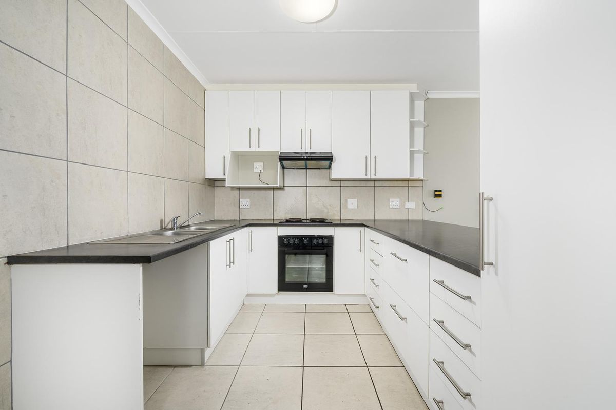 A clean, functional kitchen featuring white cabinetry, dark countertops, tiled splashbacks, and built-in oven with extractor fan.