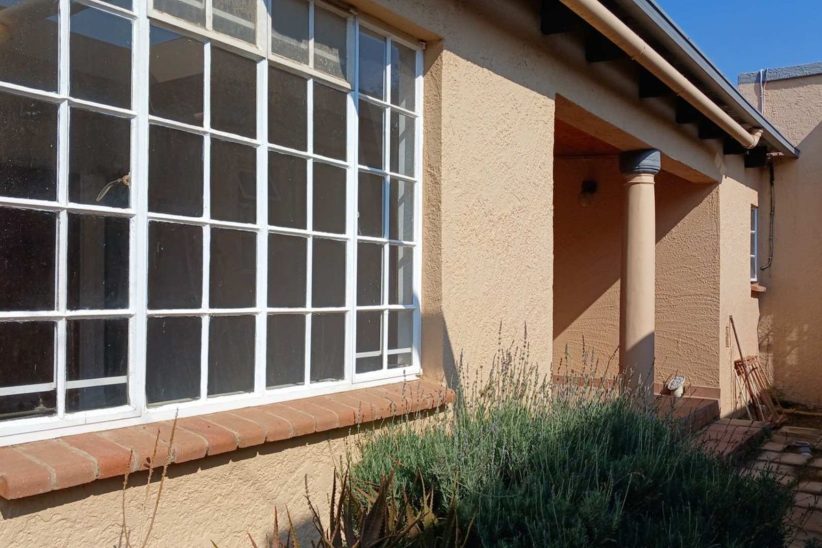 A view of the cottage rear exterior featuring a covered patio area, multi-pane windows with brick sills, and textured stucco wall finishes.