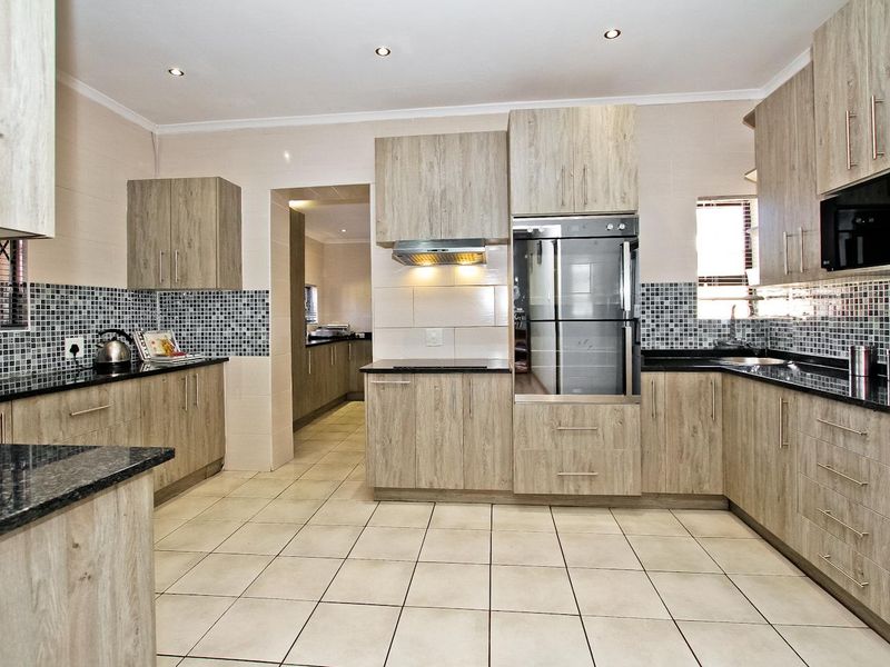 Modern kitchen featuring light wood-grain cabinetry, granite countertops, mosaic tile backsplash, and integrated appliances with tiled flooring and recessed lighting.