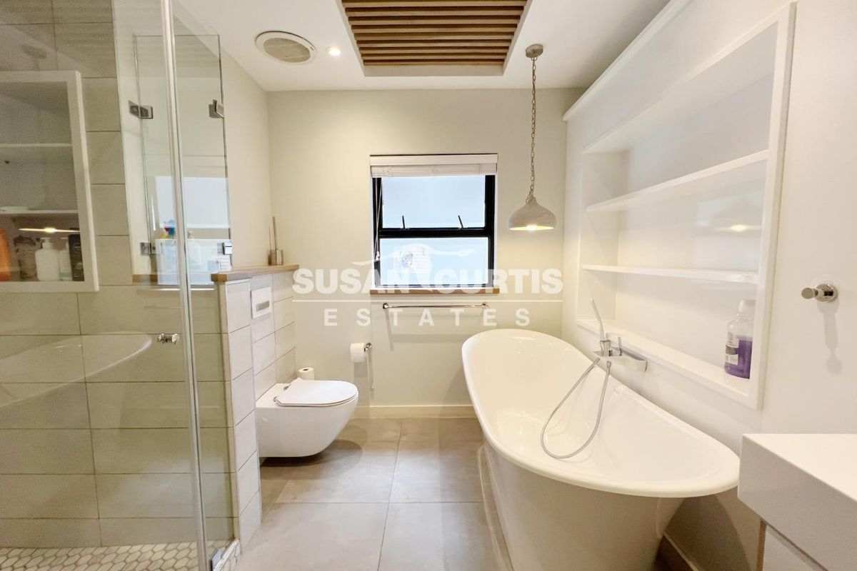 Modern bathroom featuring a freestanding bathtub, glass-enclosed shower, wall-mounted toilet, and built-in shelving with elegant timber ceiling detailing.