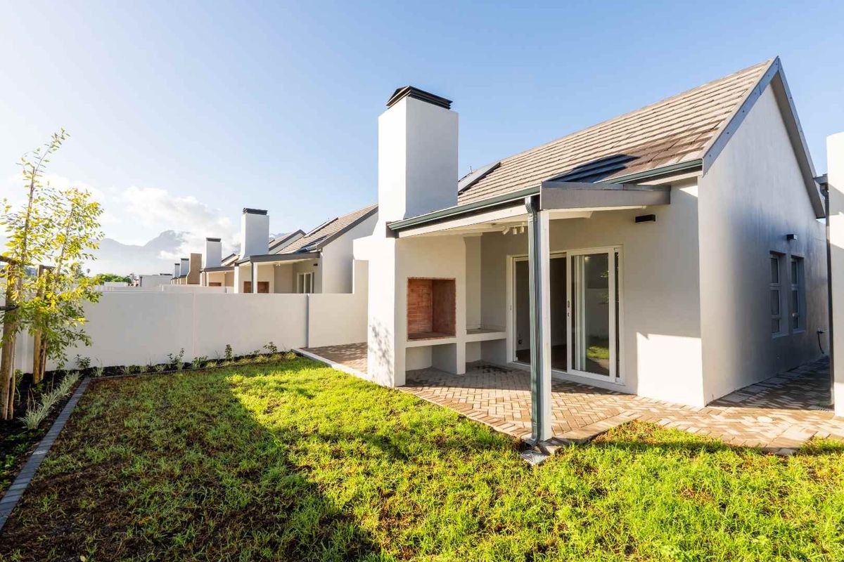 Rear view of the property featuring a paved patio with a built-in braai, sliding door access, and a well-maintained garden area.