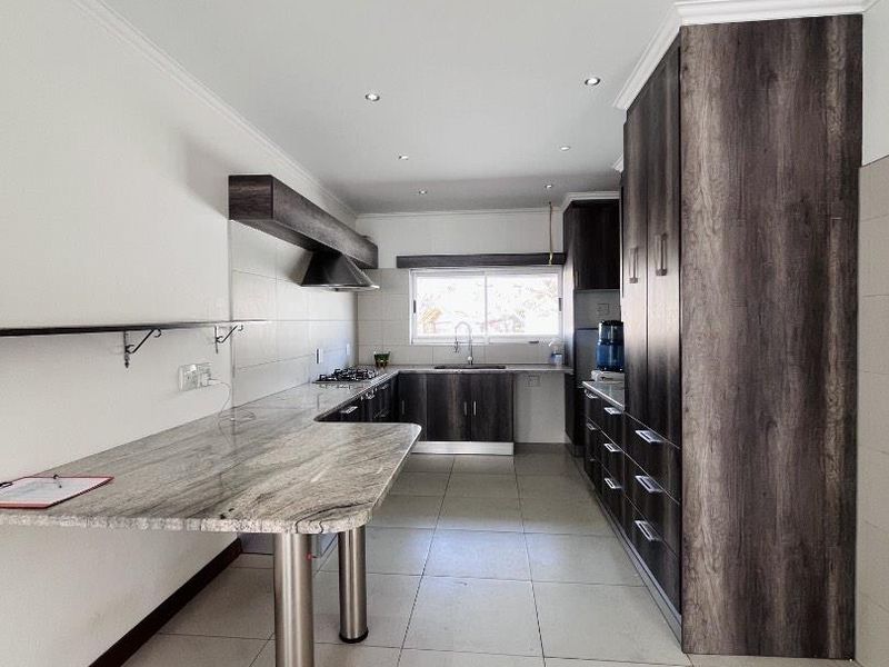 Modern kitchen featuring dark wood cabinetry, granite countertops, a gas hob with extractor, and tiled flooring in a clean, open layout.