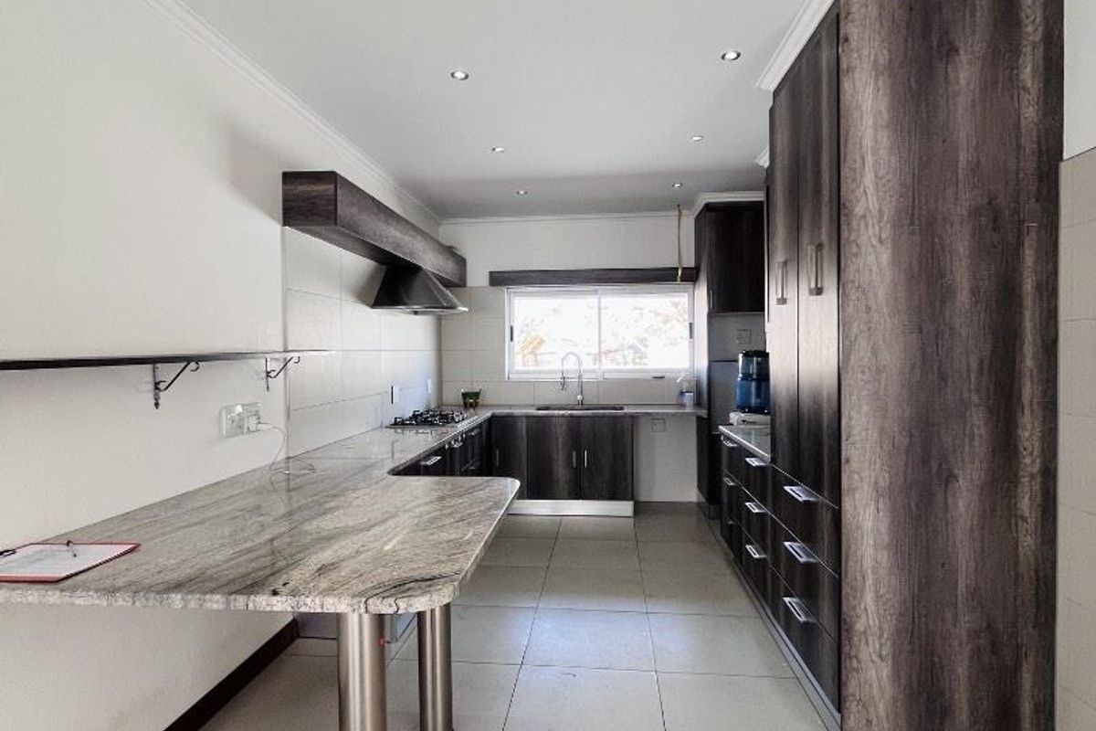 Modern kitchen featuring dark wood cabinetry, granite countertops, a gas hob with extractor, and tiled flooring in a clean, open layout.