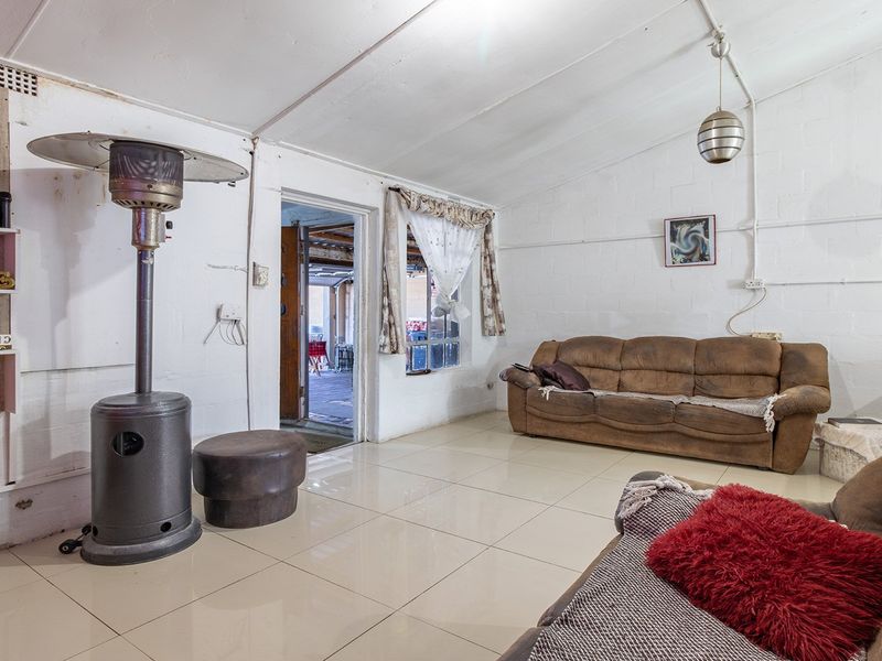 A living room featuring tiled flooring, exposed painted brick walls, and exposed electrical conduit, offering a functional space with potential for cosmetic updates.