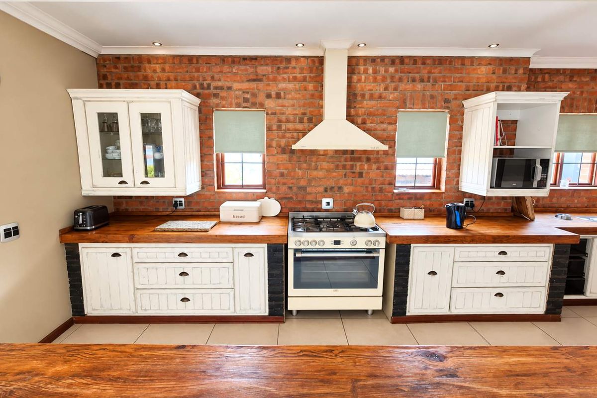 A well-maintained kitchen featuring exposed brick walls, wooden countertops, white cabinetry, and a built-in gas stove with an extractor fan.