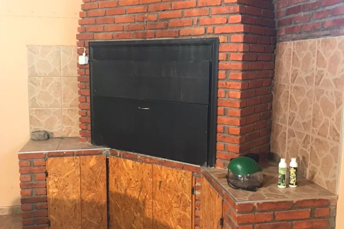 Indoor built-in brick braai or fireplace area featuring a large metal firebox, tiled countertops, and rustic wooden cabinetry.