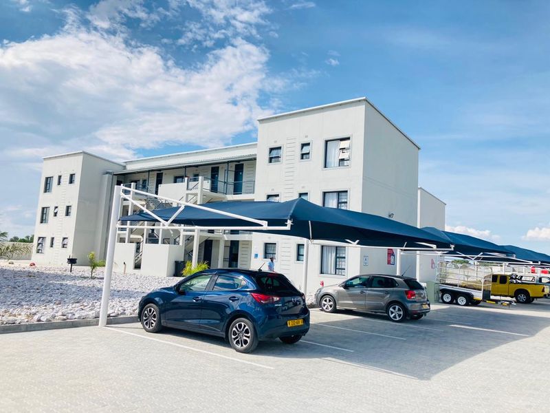Exterior view of a modern apartment complex featuring a paved parking area with shade cloth carports and multi-level building access.