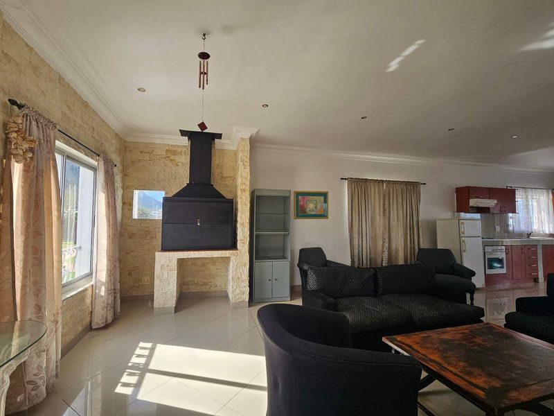 Spacious open-plan living area featuring a prominent stone-clad built-in fireplace, tiled flooring, and an integrated kitchen with wooden cabinetry.