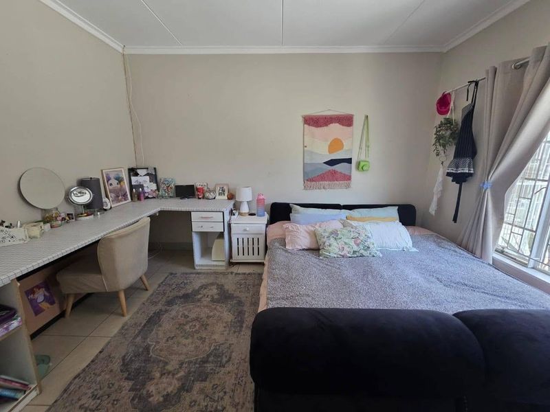 A bedroom featuring tiled flooring, a built-in desk area, and a window fitted with security bars.