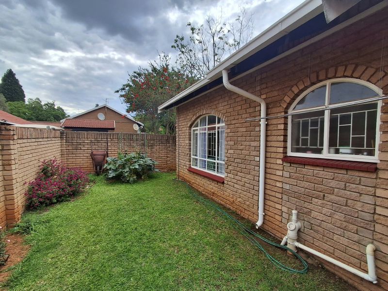 A rear exterior view of the townhouse featuring face brick walls, arched windows with security bars, and a private garden area with boundary walling.