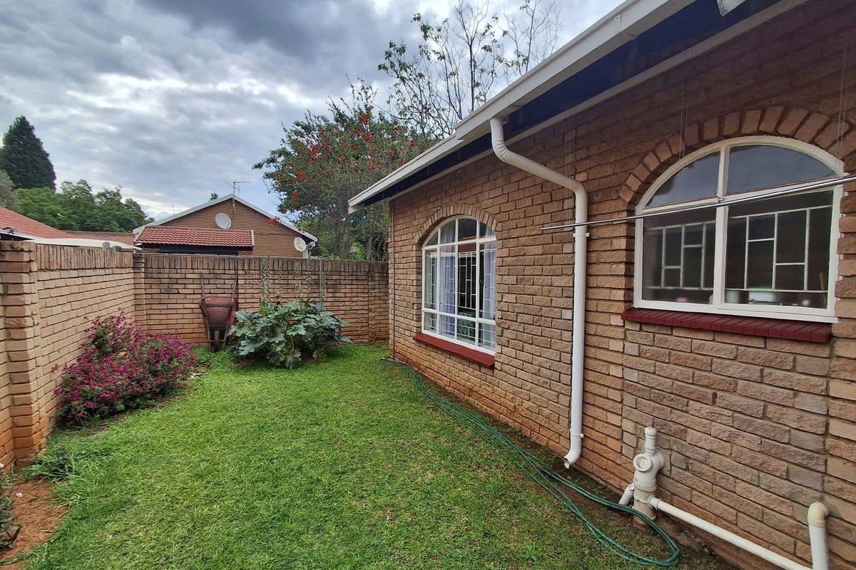 A rear exterior view of the townhouse featuring face brick walls, arched windows with security bars, and a private garden area with boundary walling.