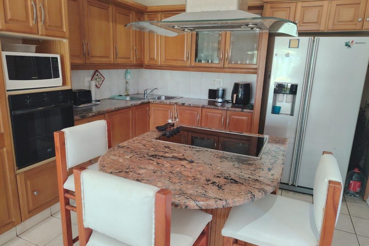 A functional kitchen featuring wooden cabinetry, granite countertops, a central island with an integrated hob, and built-in appliances including an oven and microwave.