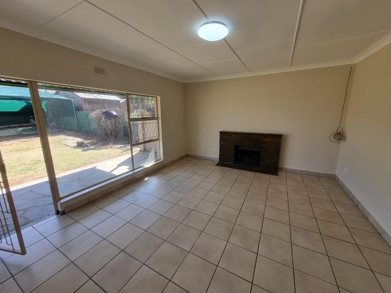 Spacious living room featuring tiled flooring, a stone fireplace, and a large sliding glass door providing direct access to the garden.