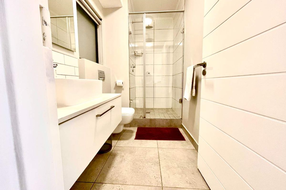 Modern bathroom featuring a glass-enclosed shower, wall-mounted vanity with basin, and neutral floor tiling.