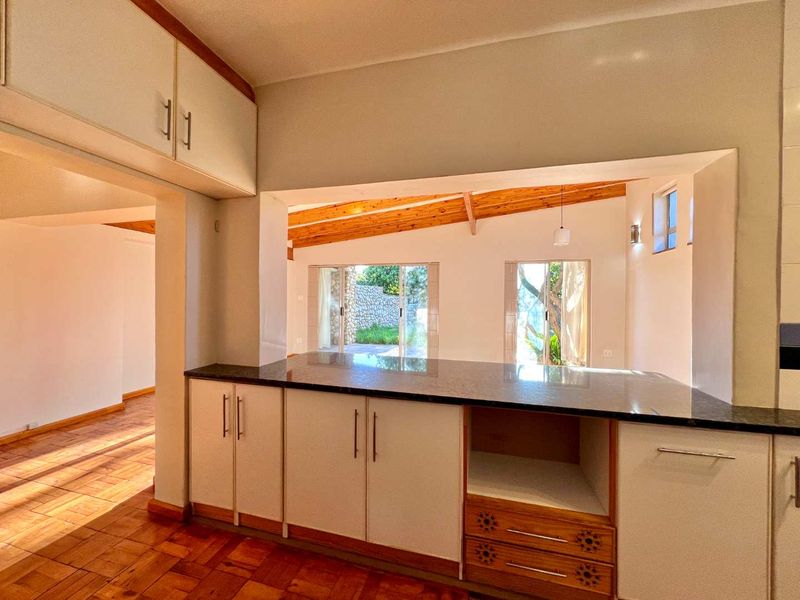 Open-plan kitchen and living area featuring parquet flooring, exposed timber ceiling beams, and a functional pass-through window connecting the spaces.