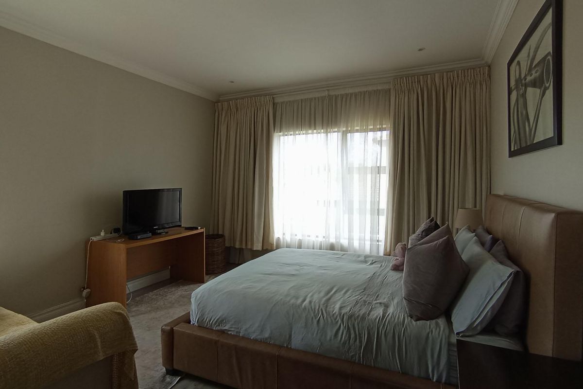 A spacious bedroom featuring neutral wall tones, large windows with floor-to-ceiling curtains, and crown molding detail.