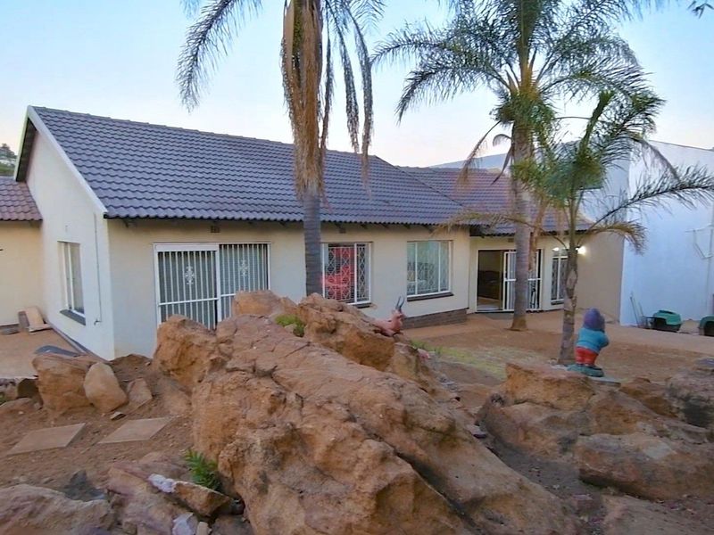 Rear view of the house featuring a tiled roof, sliding doors with security gates, and a natural rocky garden area.
