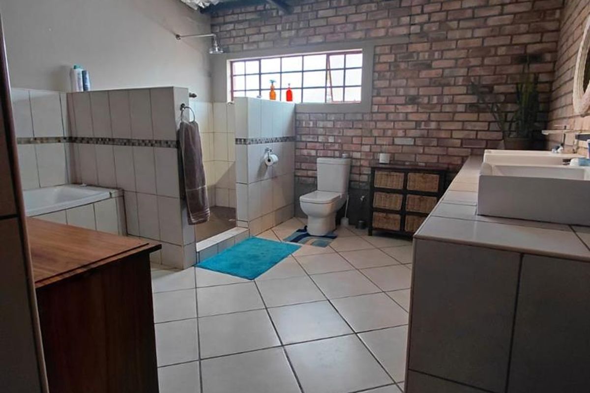 Spacious industrial-style bathroom featuring exposed brick walls, tiled flooring, a walk-in shower, a built-in bathtub, and a dual vanity setup.