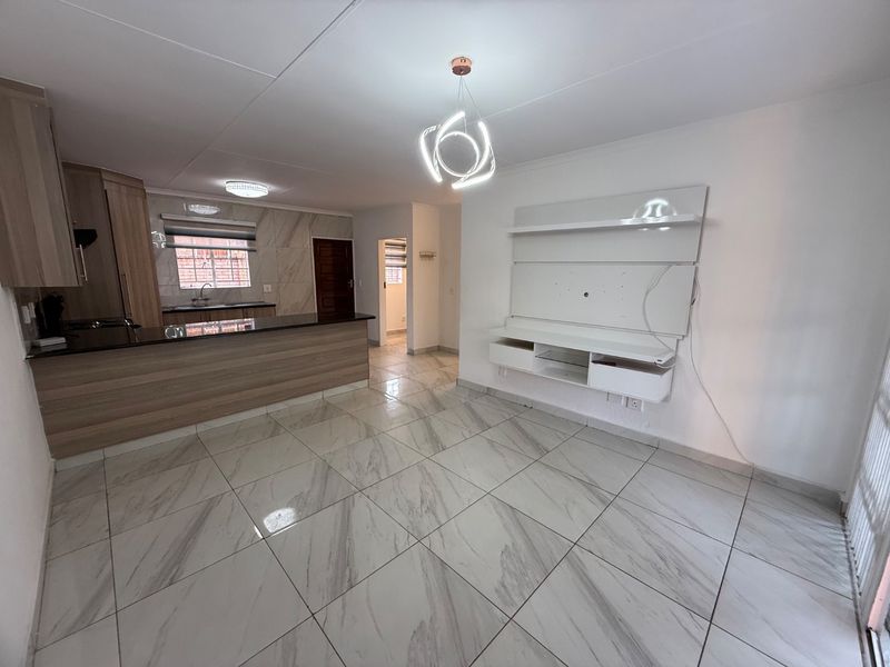 Open-plan living and kitchen area featuring marble-look floor tiles, modern cabinetry, granite countertops, and a built-in media console.