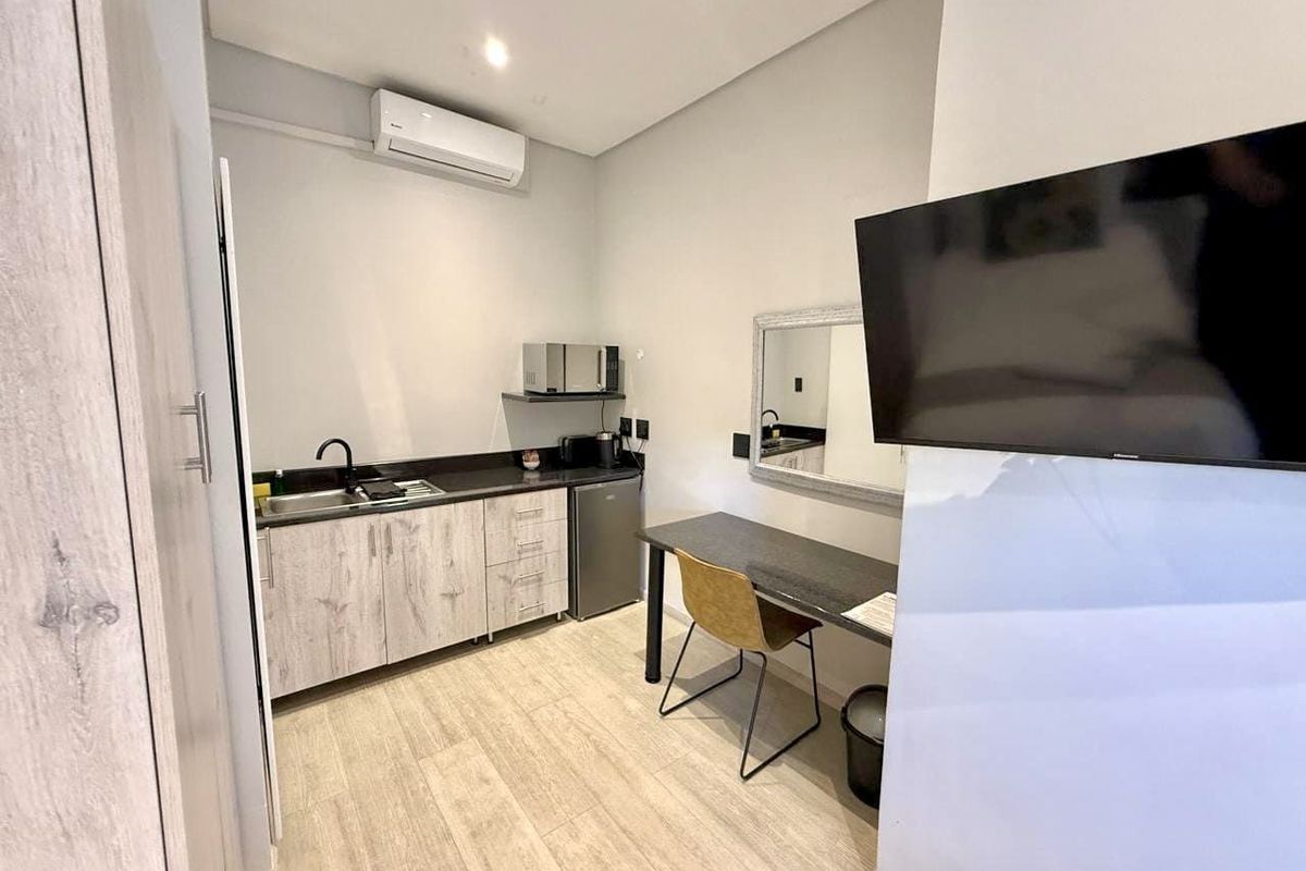 Compact kitchenette area featuring modern cabinetry, a sink, and a wall-mounted air conditioning unit.