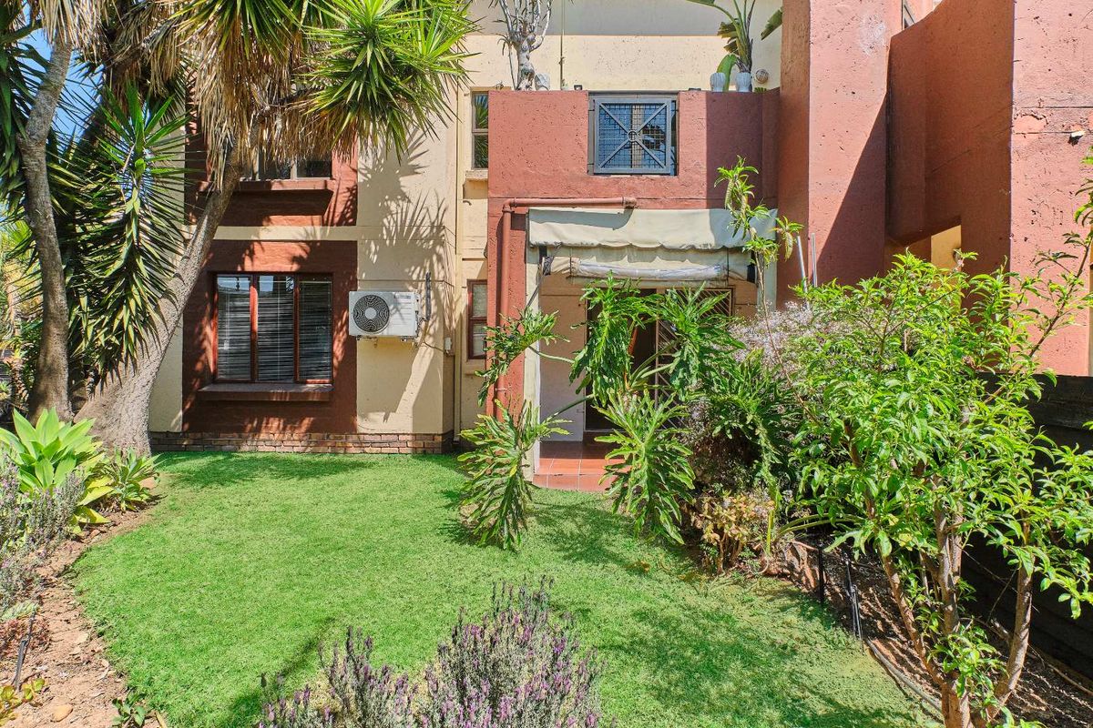 Rear view of the townhouse featuring a private garden, a small tiled patio with a retractable awning, and an exterior air conditioning unit.