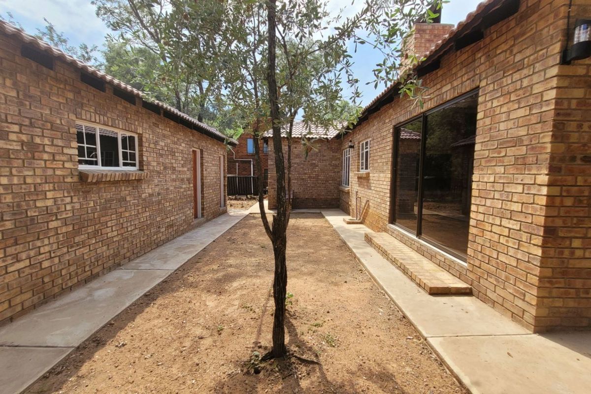 A view of the rear exterior featuring face brick walls, tiled roofing, and concrete pathways leading to sliding glass doors.