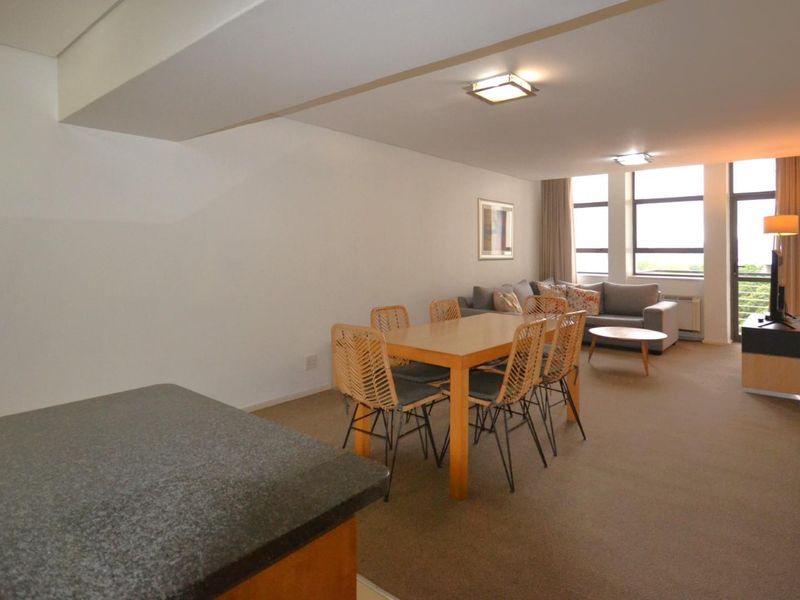 Open-plan living and dining area featuring carpeted flooring, granite kitchen counter, and large windows providing natural light.