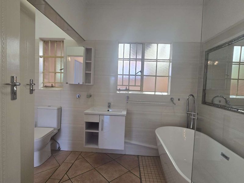 A clean and functional bathroom featuring a modern freestanding bathtub, vanity cabinet, toilet, and neutral wall and floor tiling.