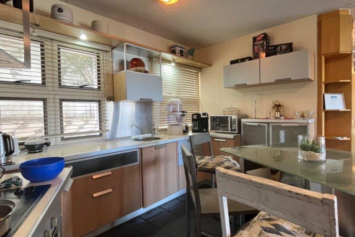 A functional kitchen featuring wood-tone cabinetry, integrated oven and hob, stone-style flooring, and ample natural light through horizontal blinds.