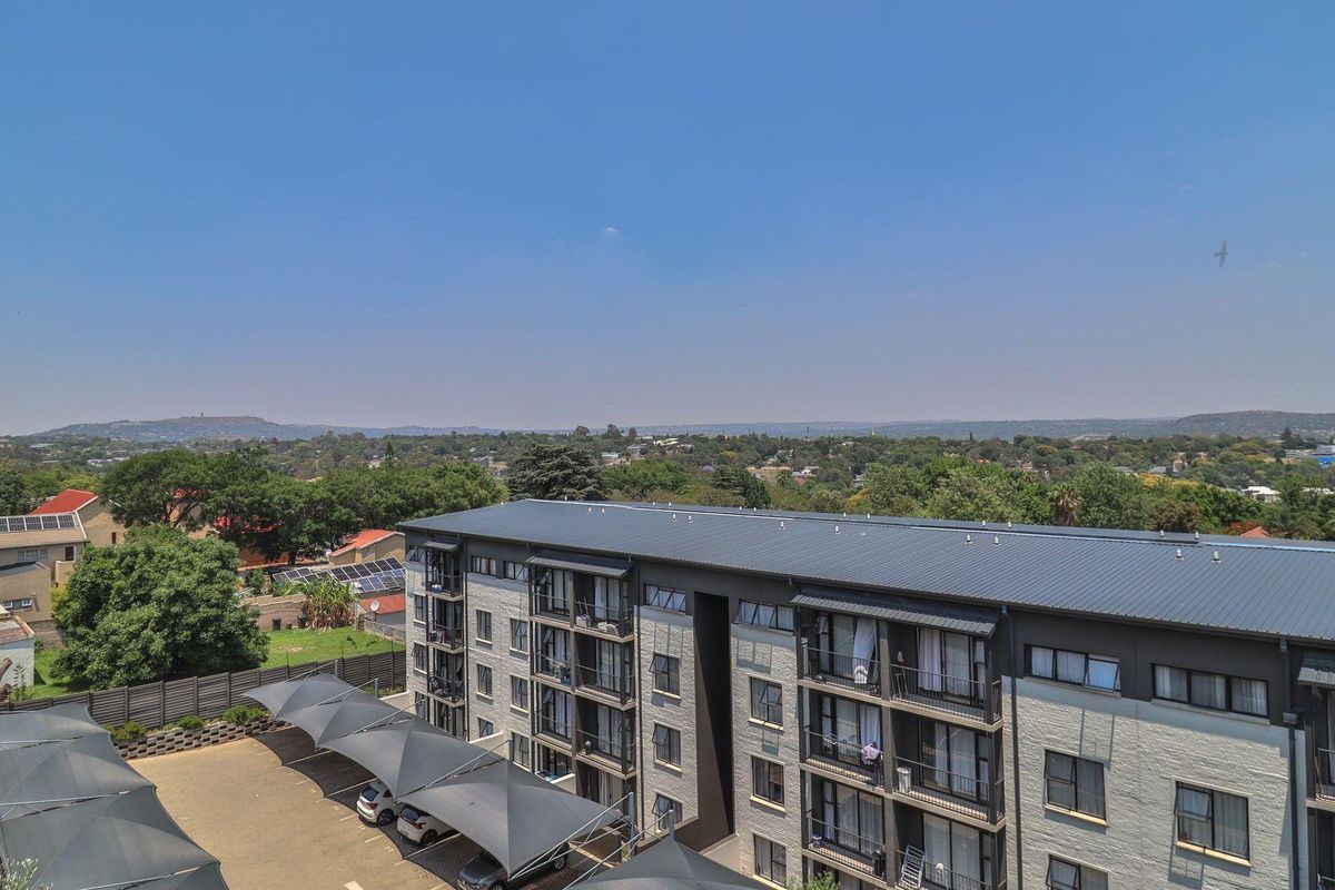 Aerial view of the apartment complex featuring a multi-story building with balconies, a paved parking area with shade cloth carports, and surrounding landscape.