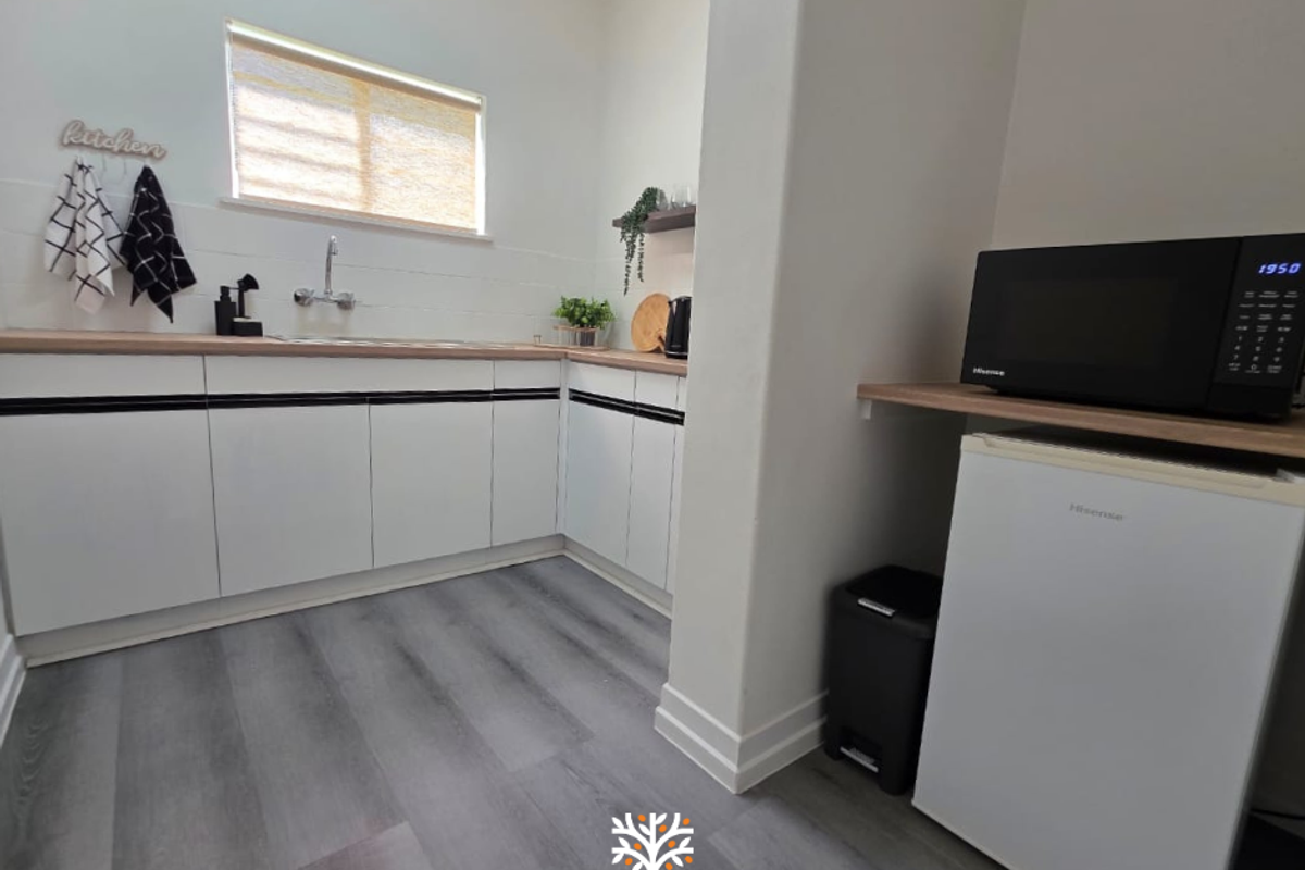 A clean, modern kitchen area featuring white cabinetry, wood-look laminate countertops, a stainless steel sink, and durable vinyl flooring.