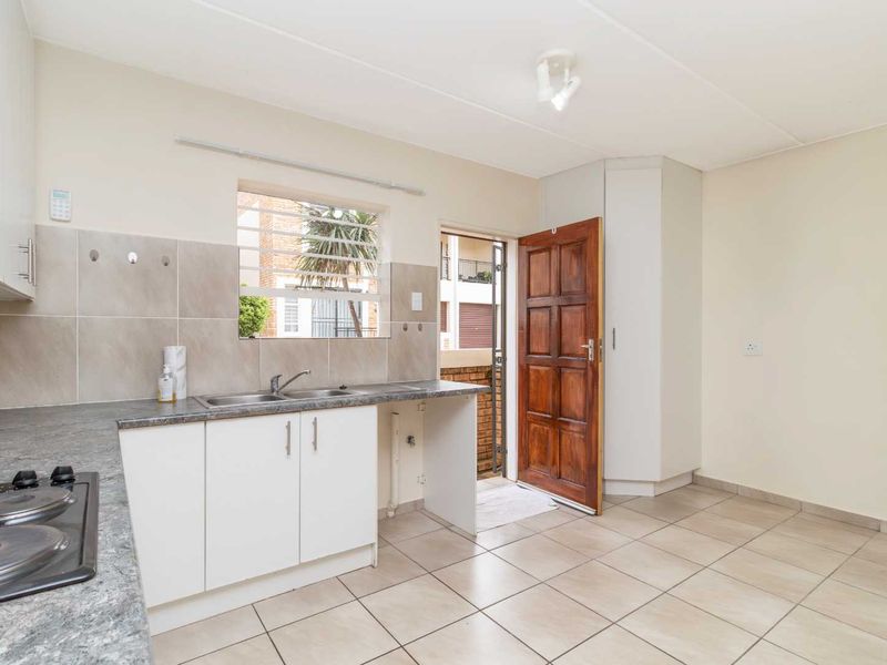 A functional kitchen featuring white cabinetry, laminate countertops, a built-in electric hob, and tiled flooring, with direct access to an exterior area.