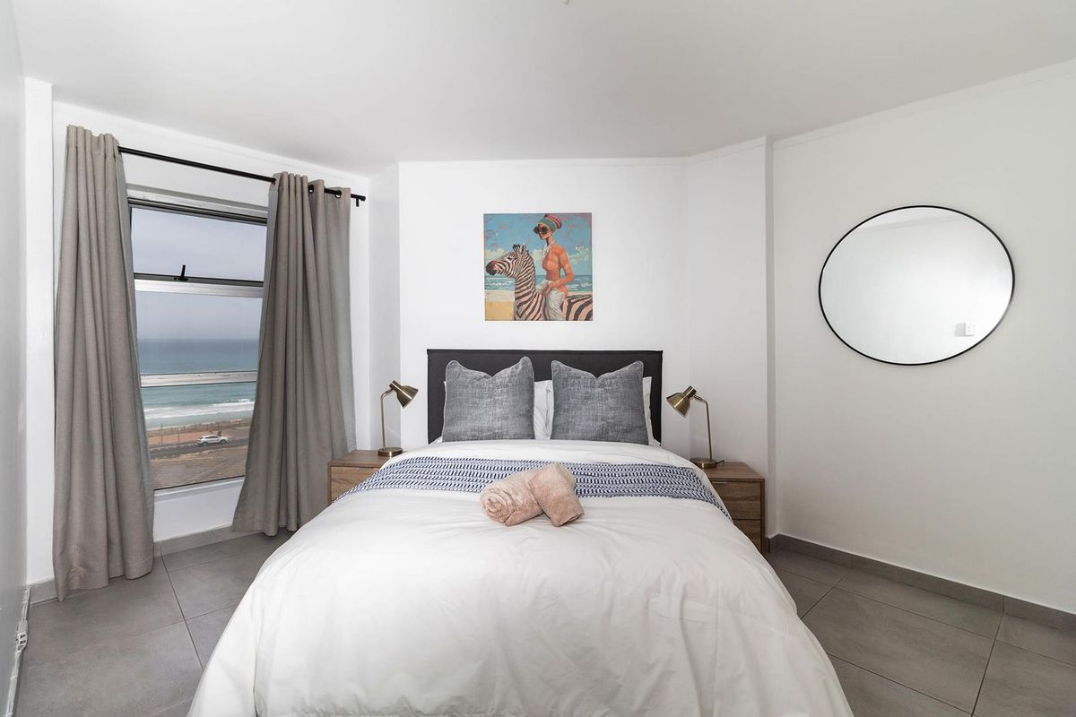 A bright bedroom featuring neutral tiled flooring and a large window offering scenic coastal views.