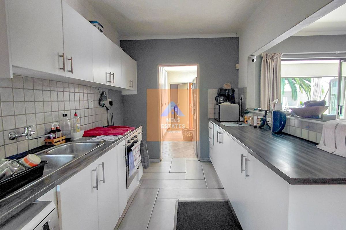 A functional galley-style kitchen featuring white cabinetry, dark laminate countertops, a double stainless steel sink, and tiled flooring.