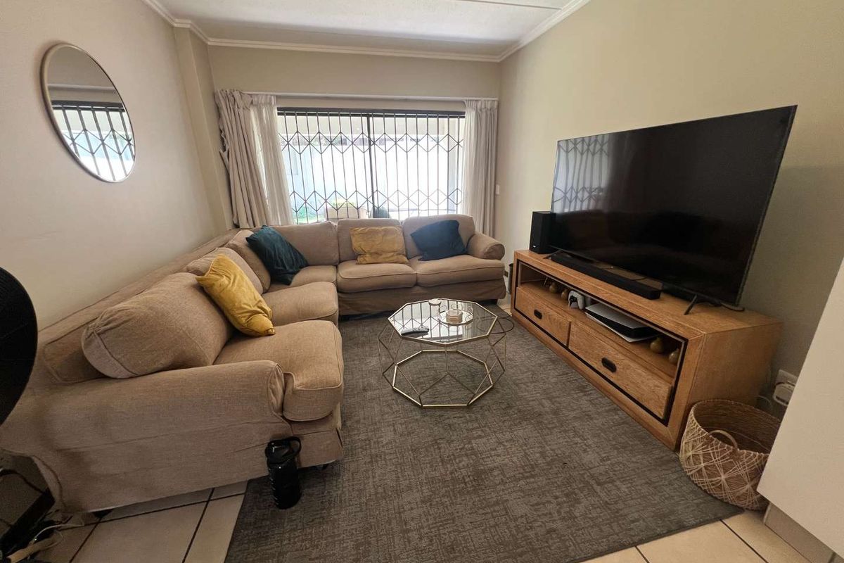 A comfortable living room featuring tiled flooring, neutral wall tones, and a large window fitted with security bars for added peace of mind.