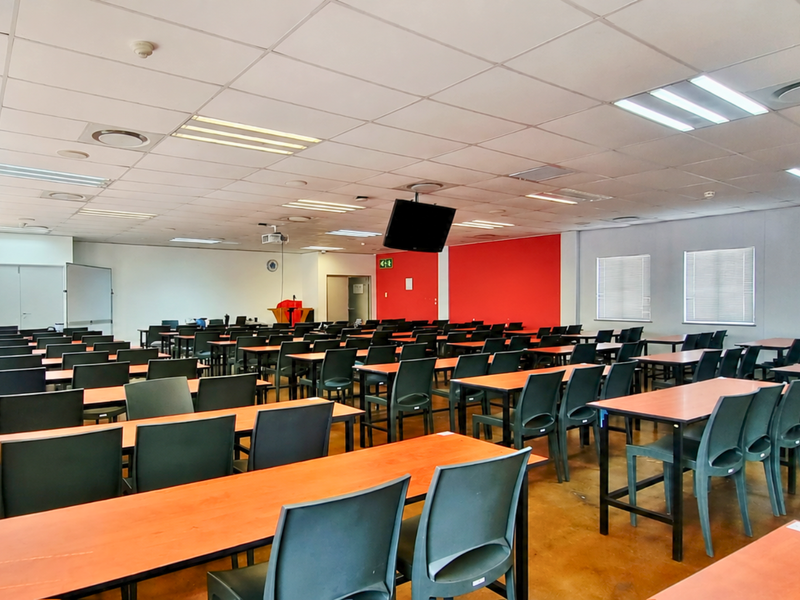 A spacious, well-lit office or training room featuring a suspended ceiling, recessed lighting, and large windows with venetian blinds.