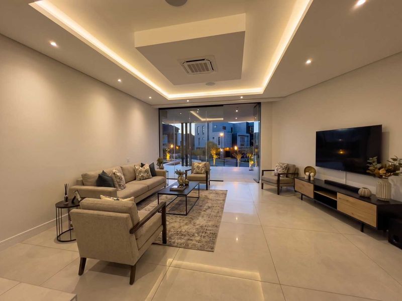 Modern living room featuring large format floor tiles, recessed ceiling with cove lighting, ducted air conditioning, and seamless access to the outdoor patio area.