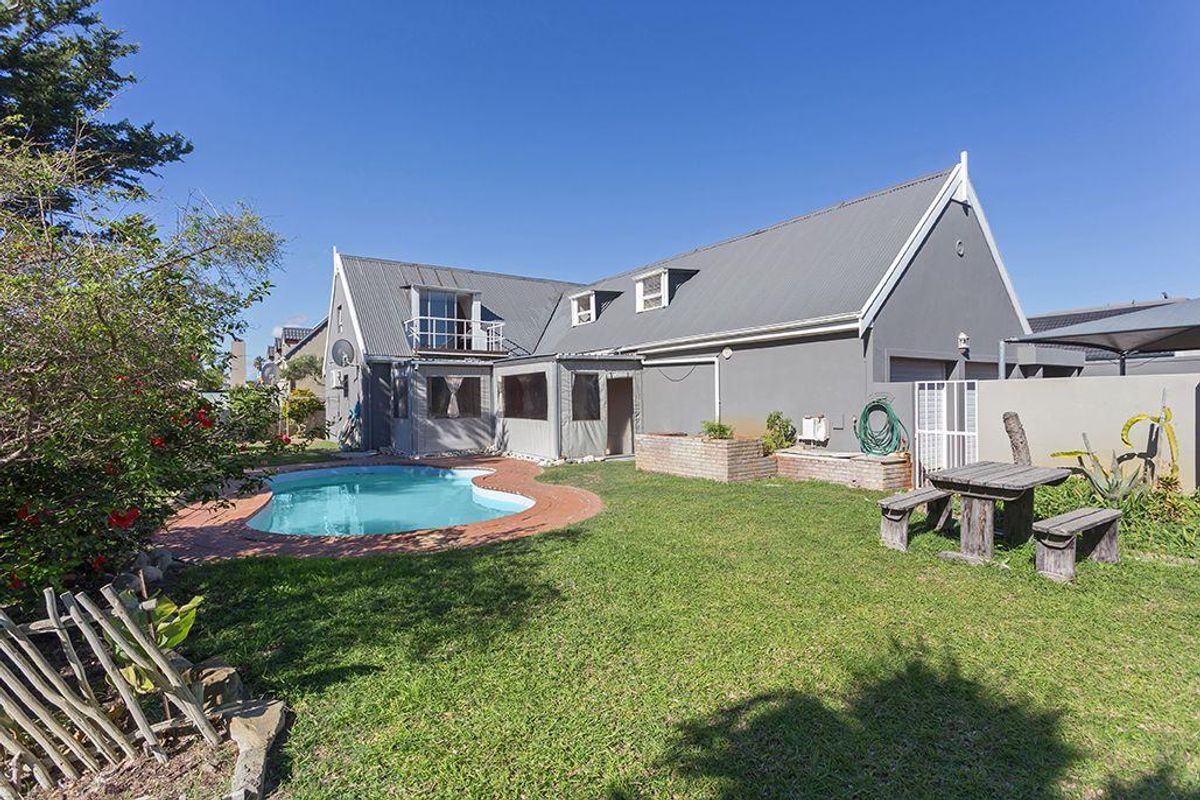Rear view of the property featuring a swimming pool, landscaped garden, covered patio area, and a balcony attached to the main house structure.