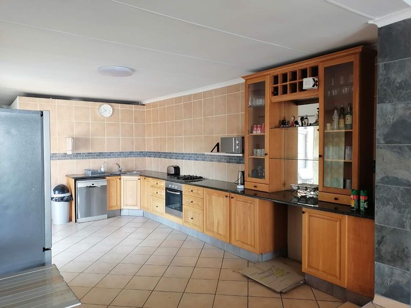 Spacious kitchen featuring wooden cabinetry, granite countertops, integrated oven, gas hob, and tiled flooring, offering a functional layout with ample storage space.