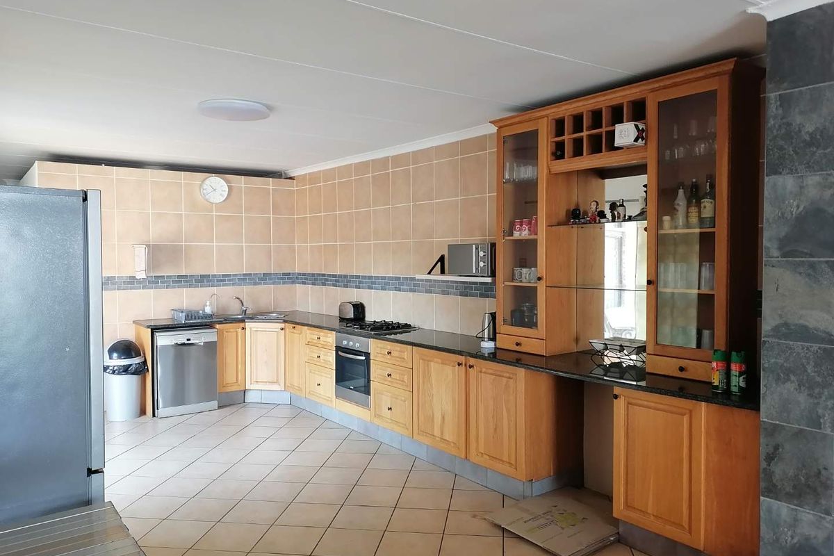 Spacious kitchen featuring wooden cabinetry, granite countertops, integrated oven, gas hob, and tiled flooring, offering a functional layout with ample storage space.